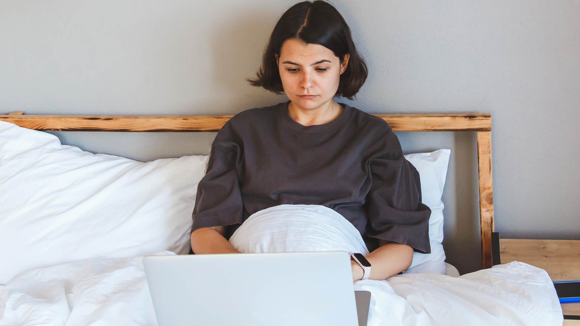Woman with no workspace or desk working from bed.