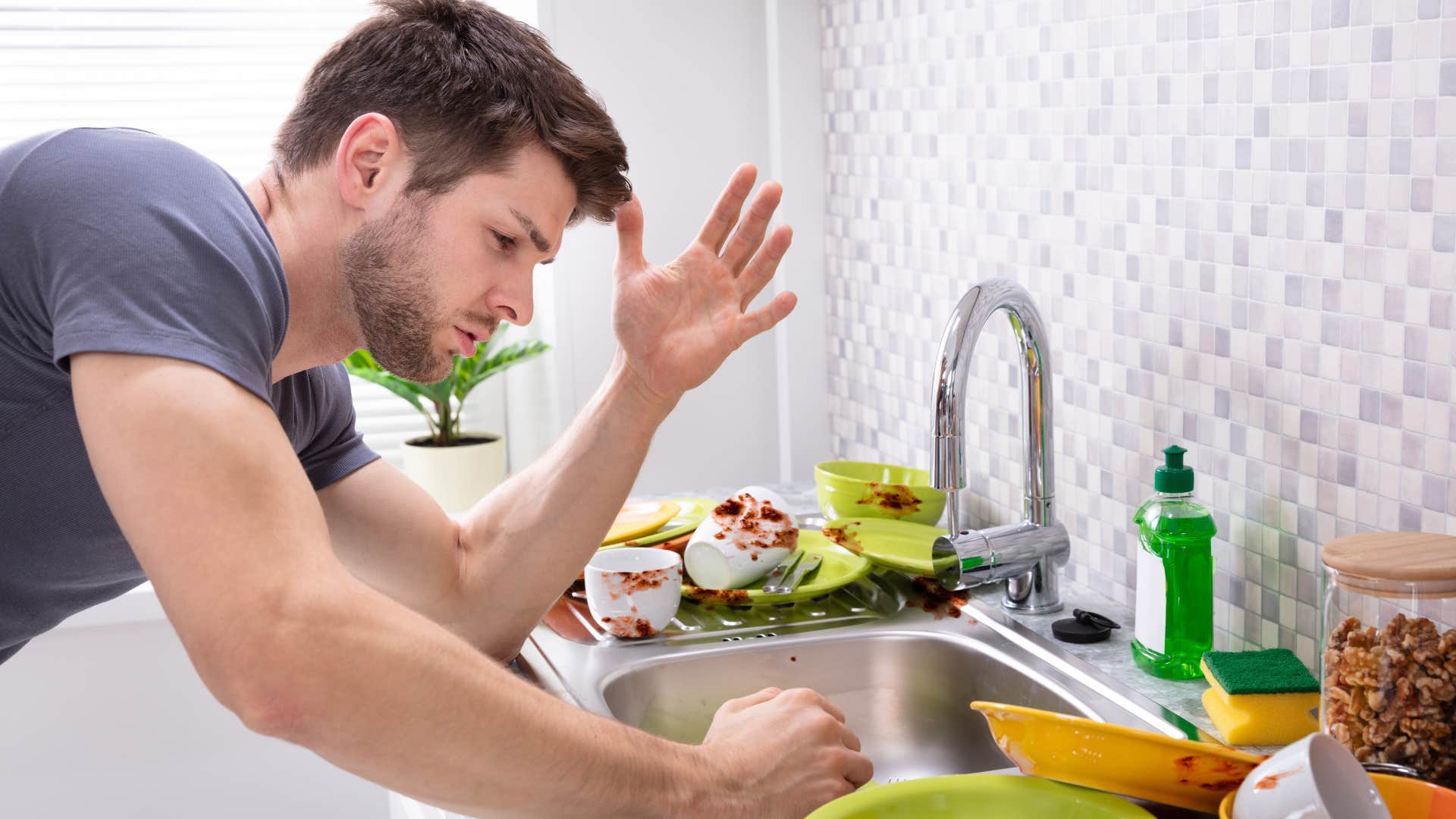 Man looking at his overflowing sink of dirty dishes.
