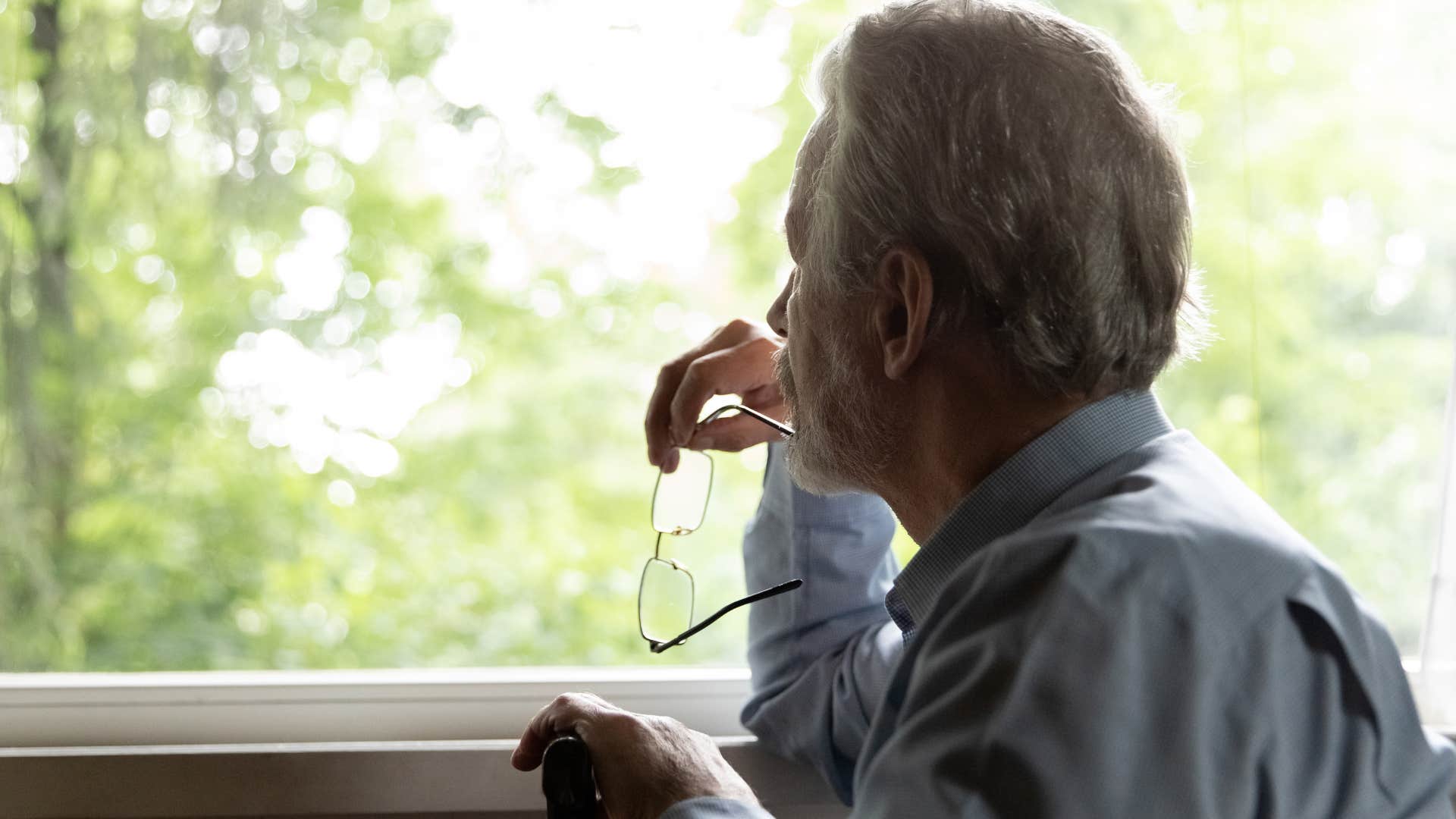 Man looking out the window at an unkept lawn and landscaping.