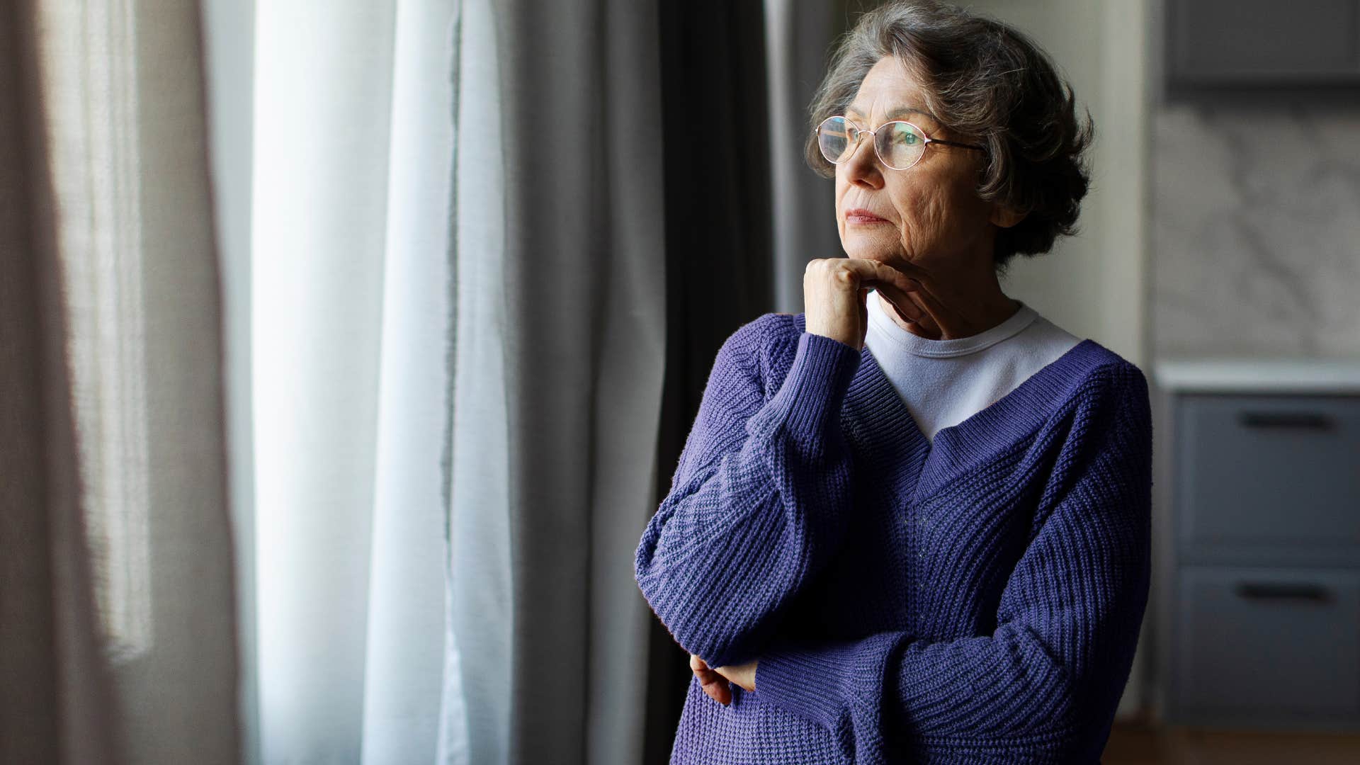 Woman whose yard is overgrown looking out her window.