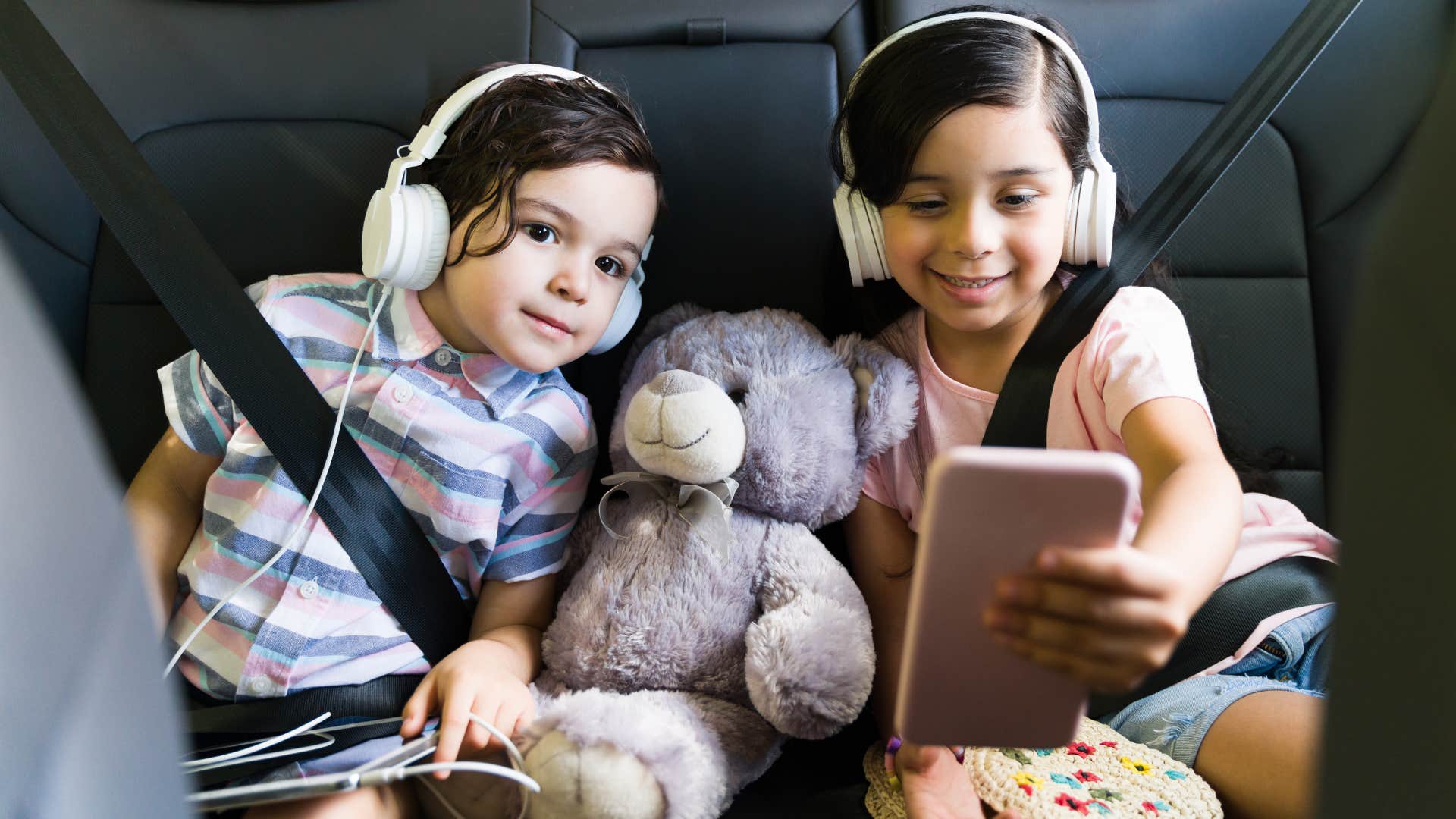 little girls smiling in a car with clothes and toys everywhere