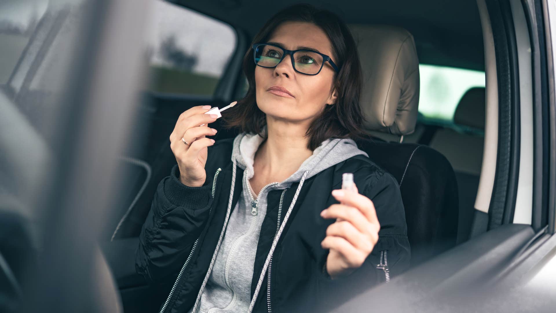woman looking in the mirror doing makeup in the car
