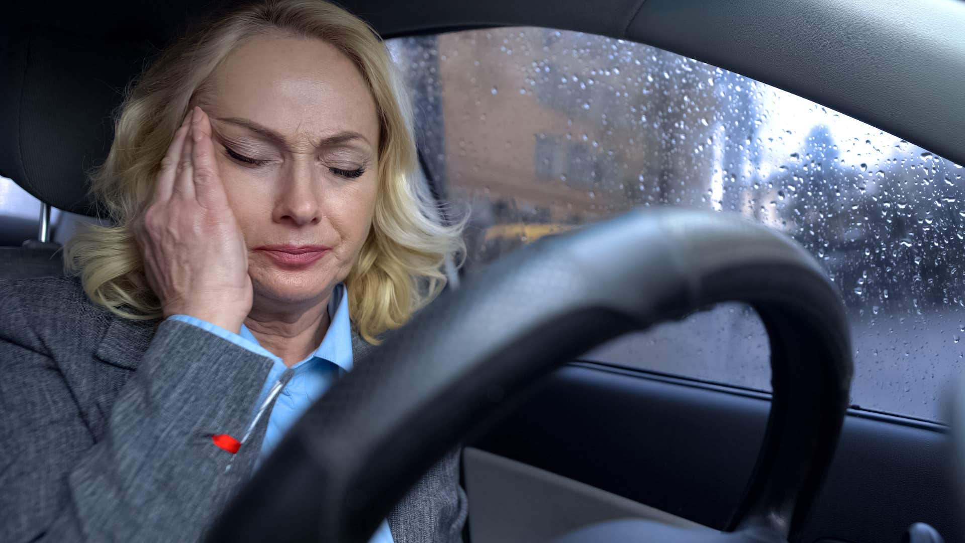 woman sitting in a car with trash and clutter around her