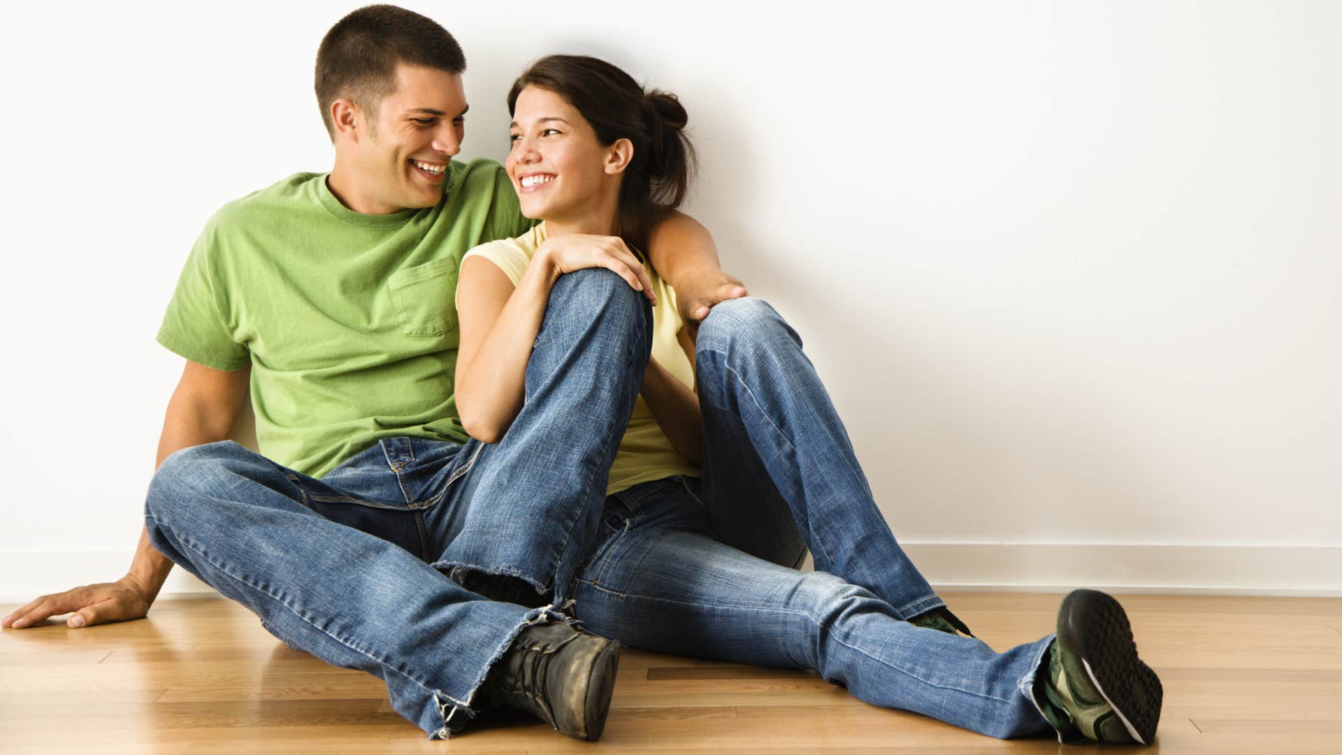 Couple smiling and sitting on hardwood flooring.