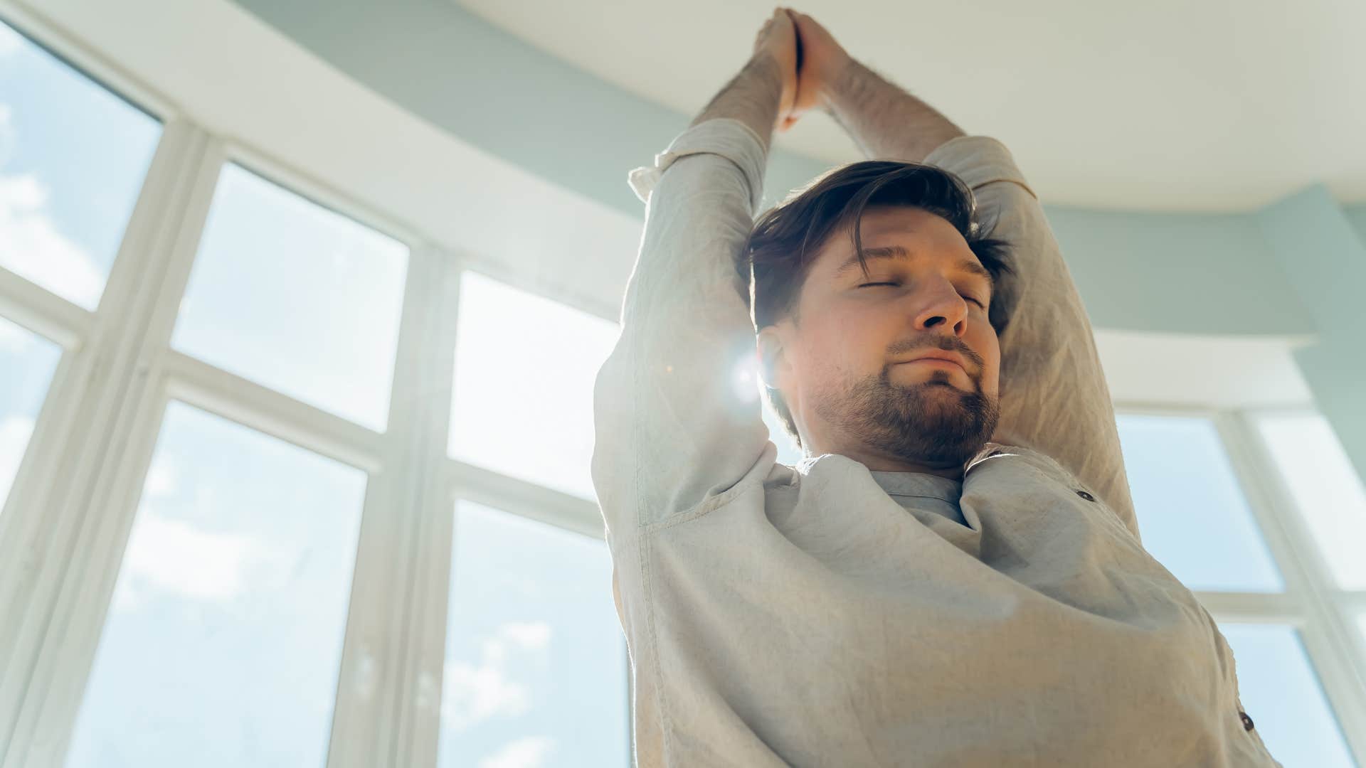 Man stretching in his home with high ceilings.