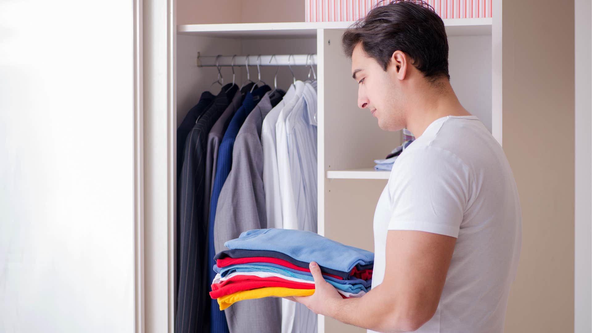 Man in his walk-in closet with a stack of clothes.