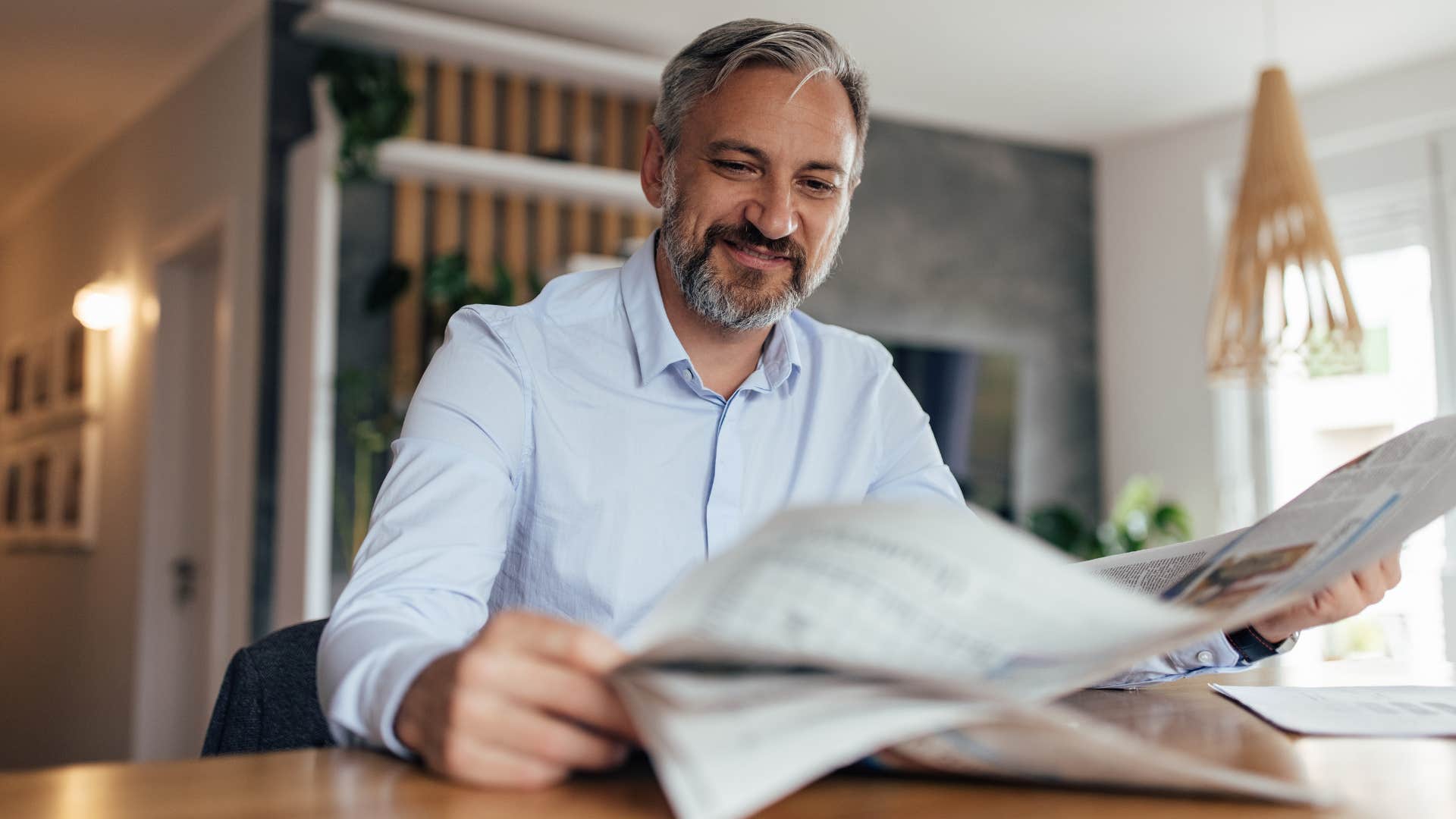 Man reading physical newspapers and magazines at home.