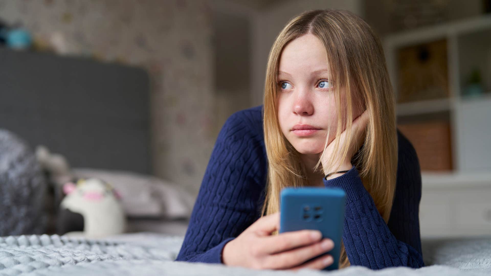teenage girl in blue shirt having unlimited screen time as she lays down with phone