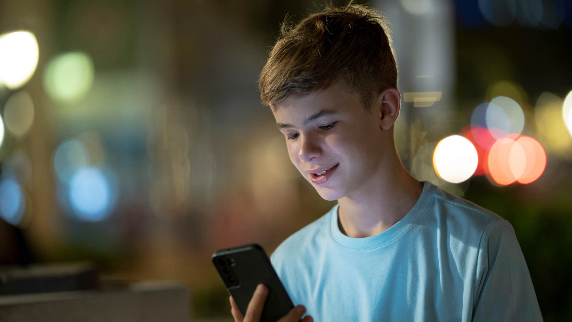 teenage boy in blue shirt ignoring curfew as he's on phone at night