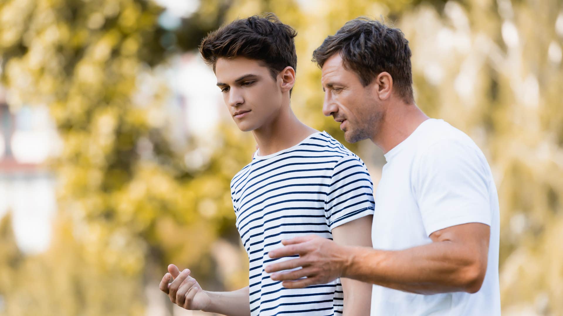 father in white shirt talking to son as he tells son to stop interrupting people mid conversation
