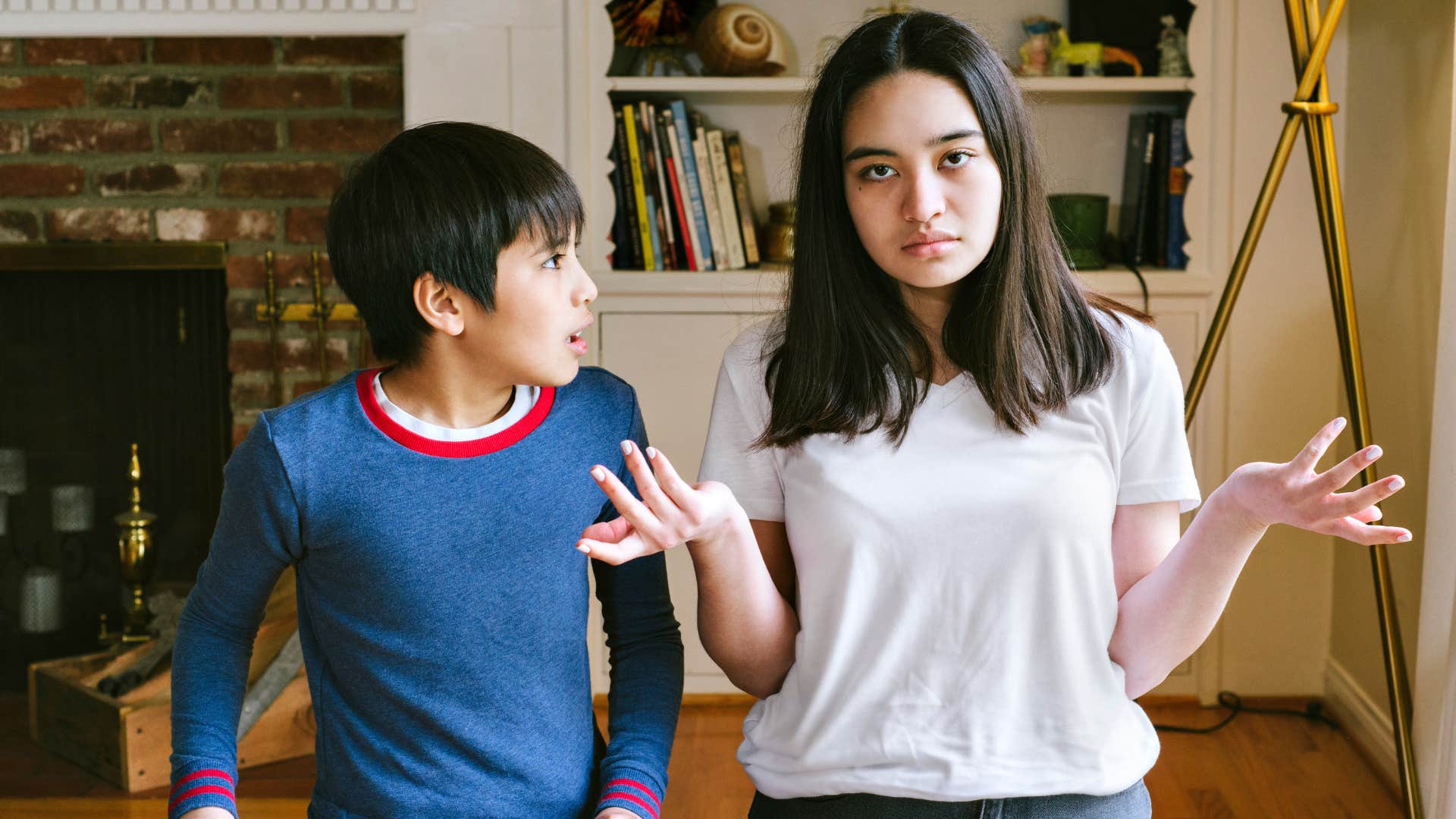 teenager in white shirt talking down to her sibling as sibling looks mad