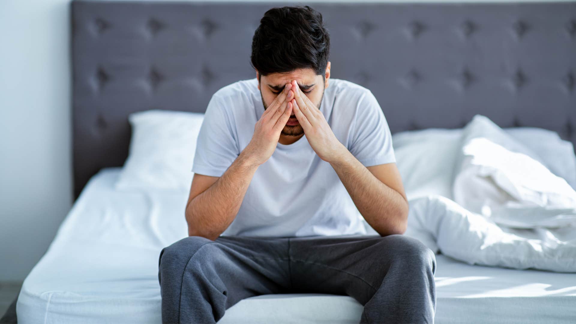 man struggles to celebrate wins as he puts head in hand while sitting on bed