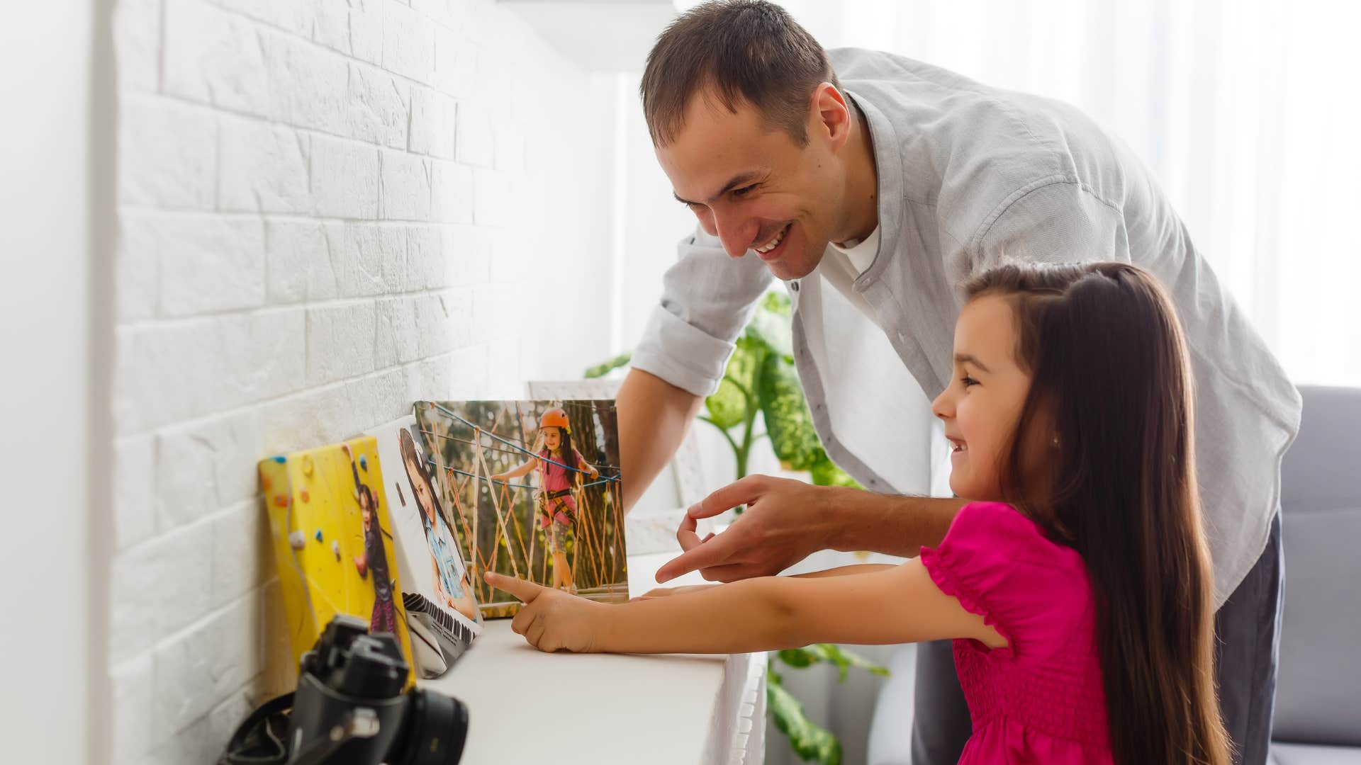 Man hanging up family photos at home with his daughter.