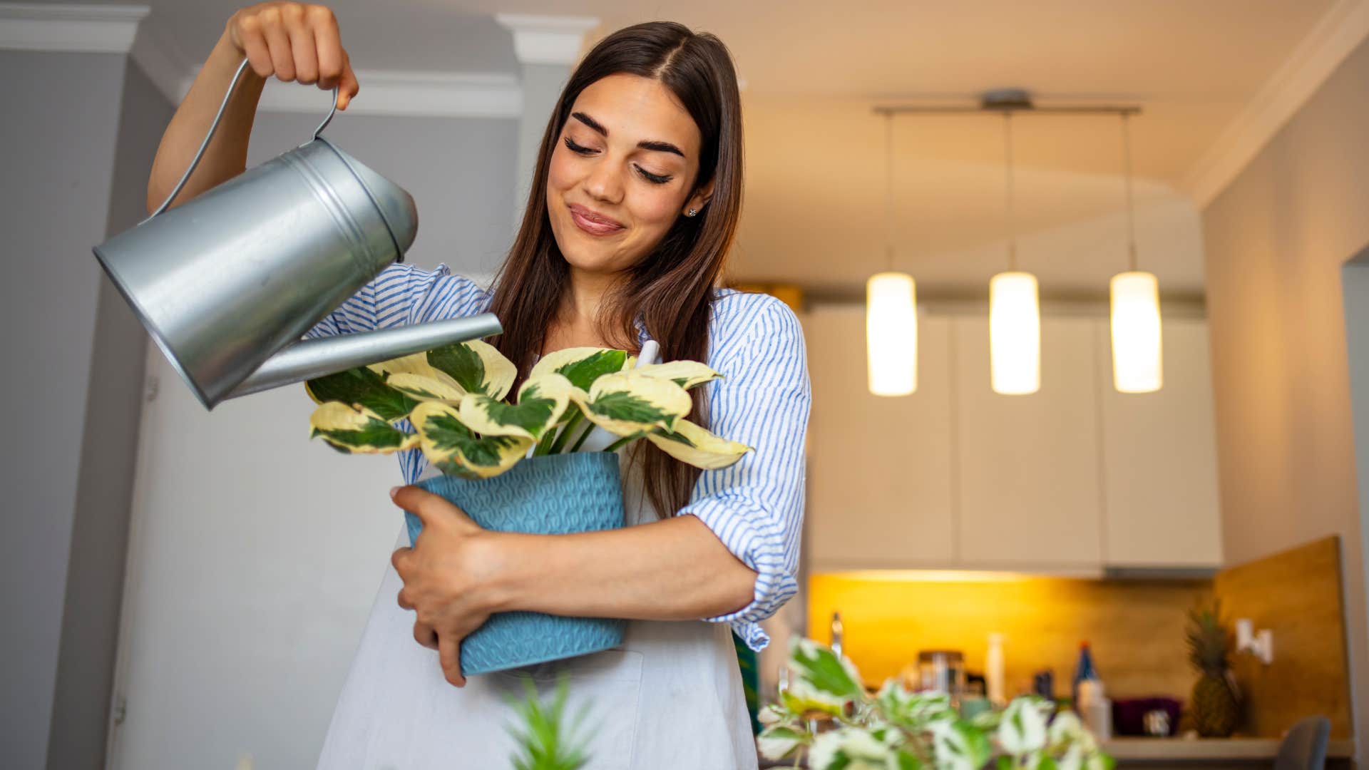 Woman smiling and watering a plant at home.
