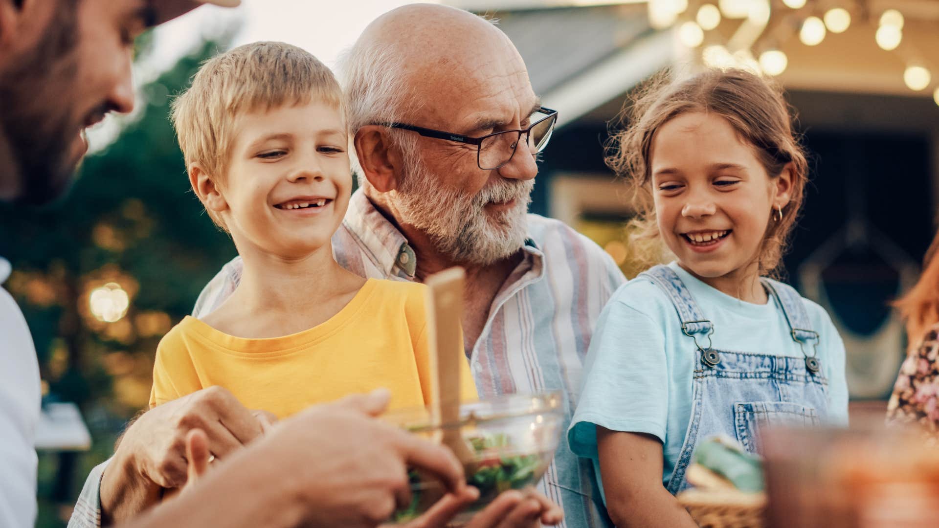 Man smiling and holding his grandchildren in a space for connection at home.