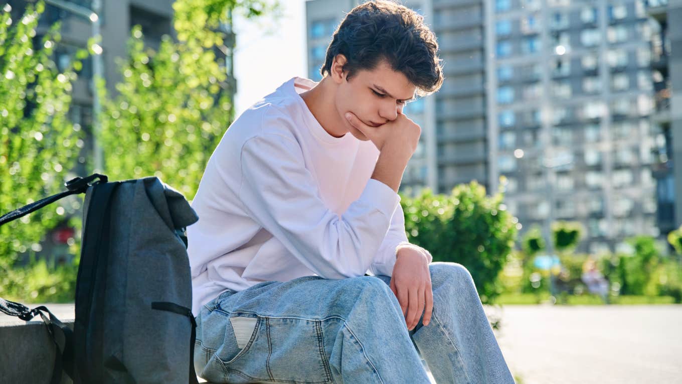 upset young man sitting on park bench outside