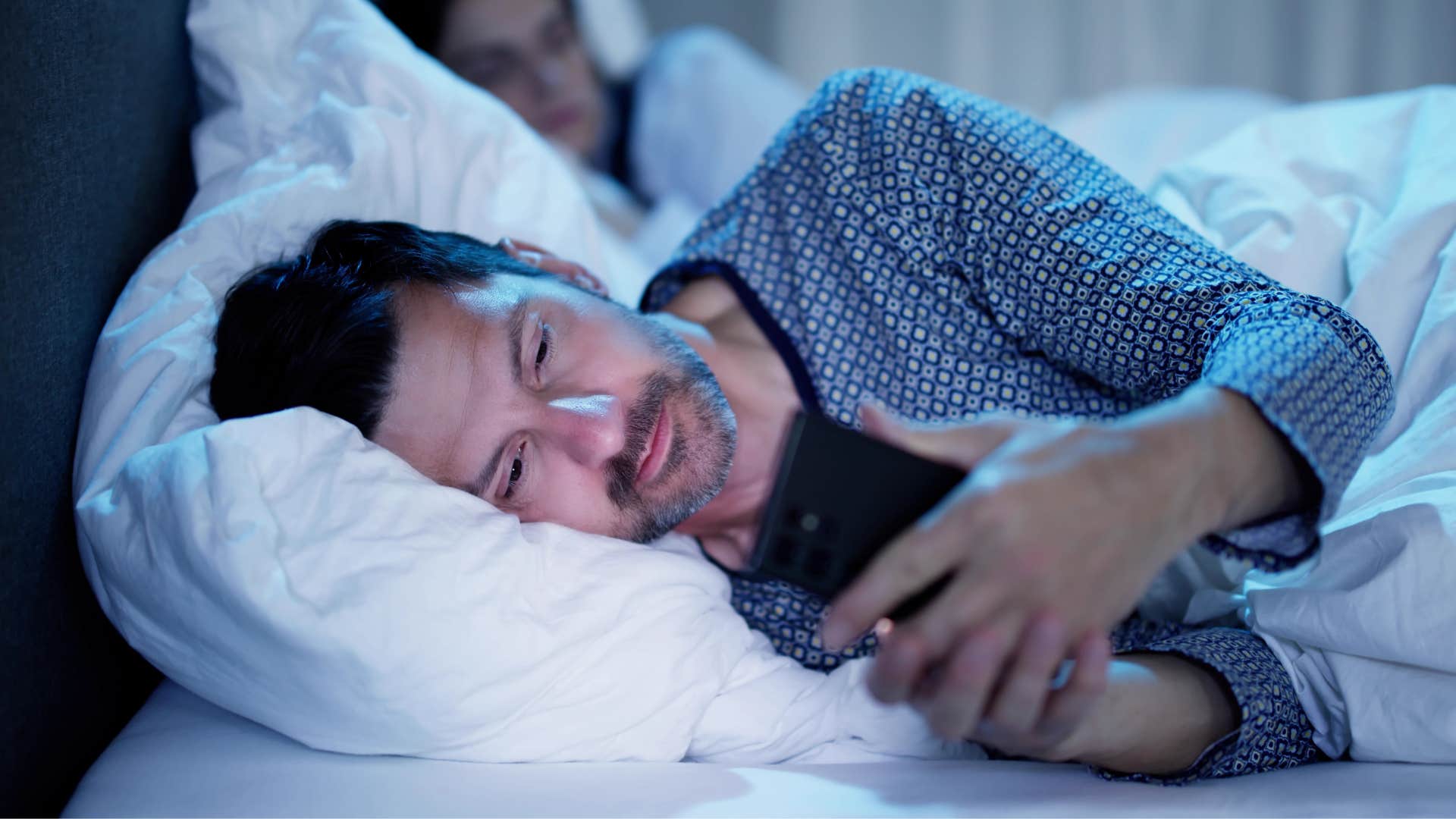 Man who cheats texting on his phone in bed.
