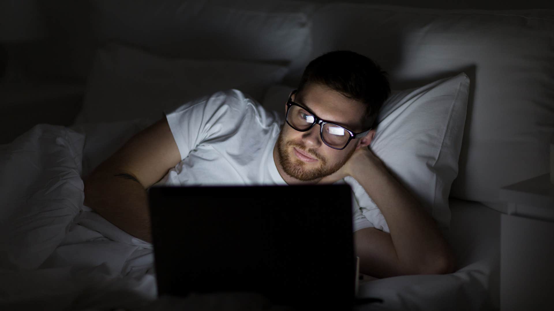 man looking up anti-aging hacks in bed on laptop