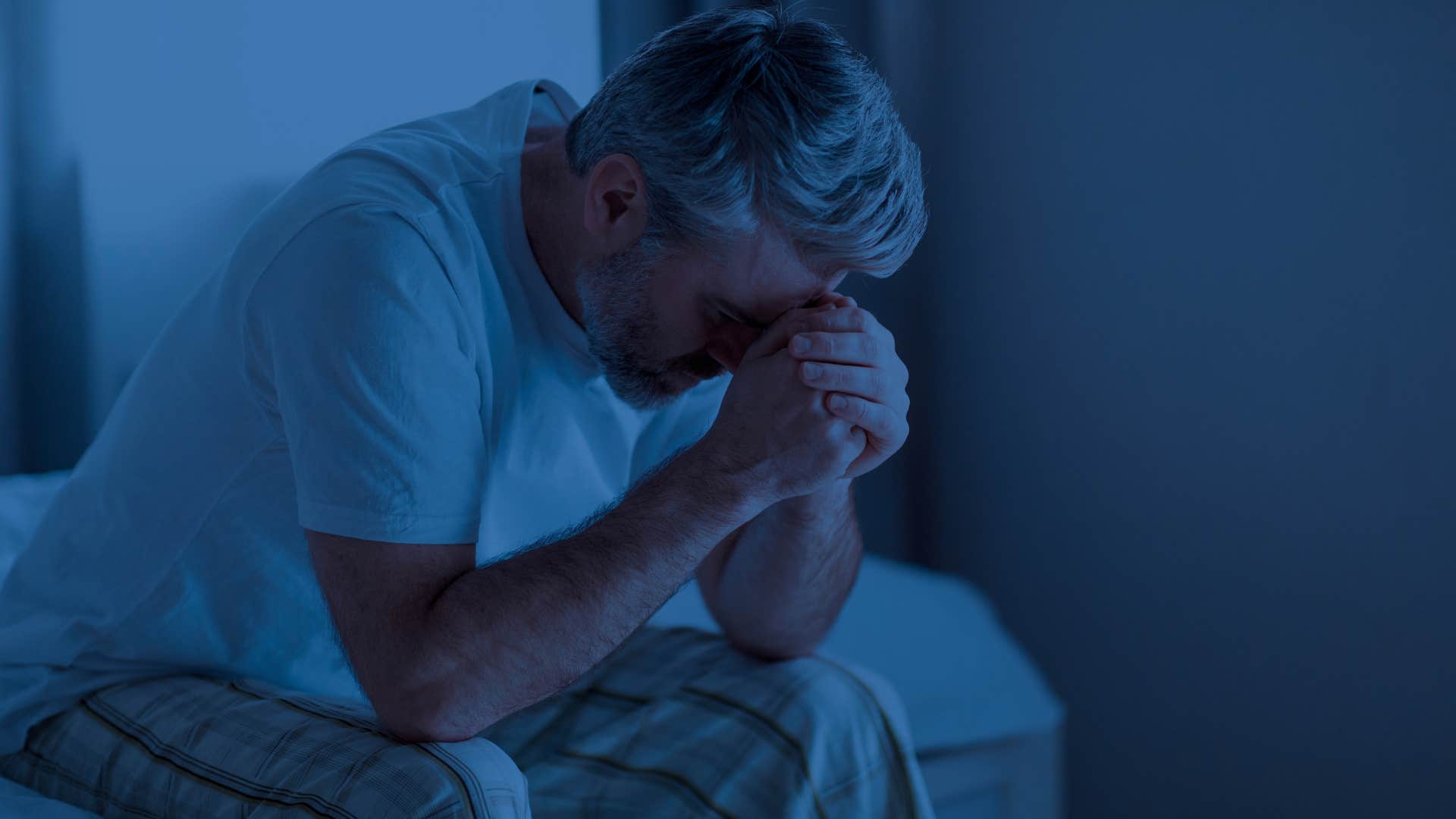 Man who goes to sleep angry sitting on his bed.