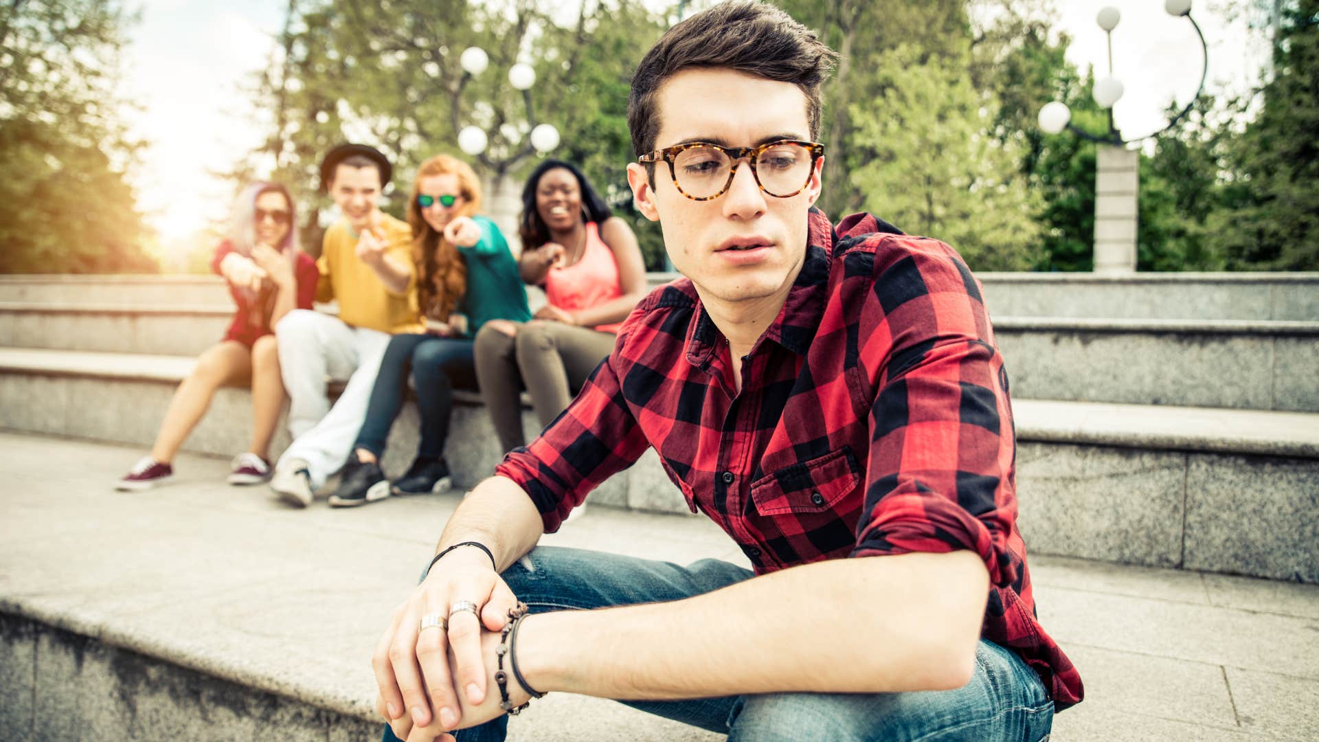 friend group making man in glasses the punchline as man looks upset and alone