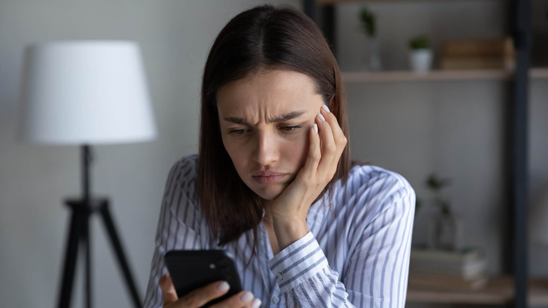 woman in stripped shirt visibility upset as she looks at phone and realizes she only hears from friends during the holidays