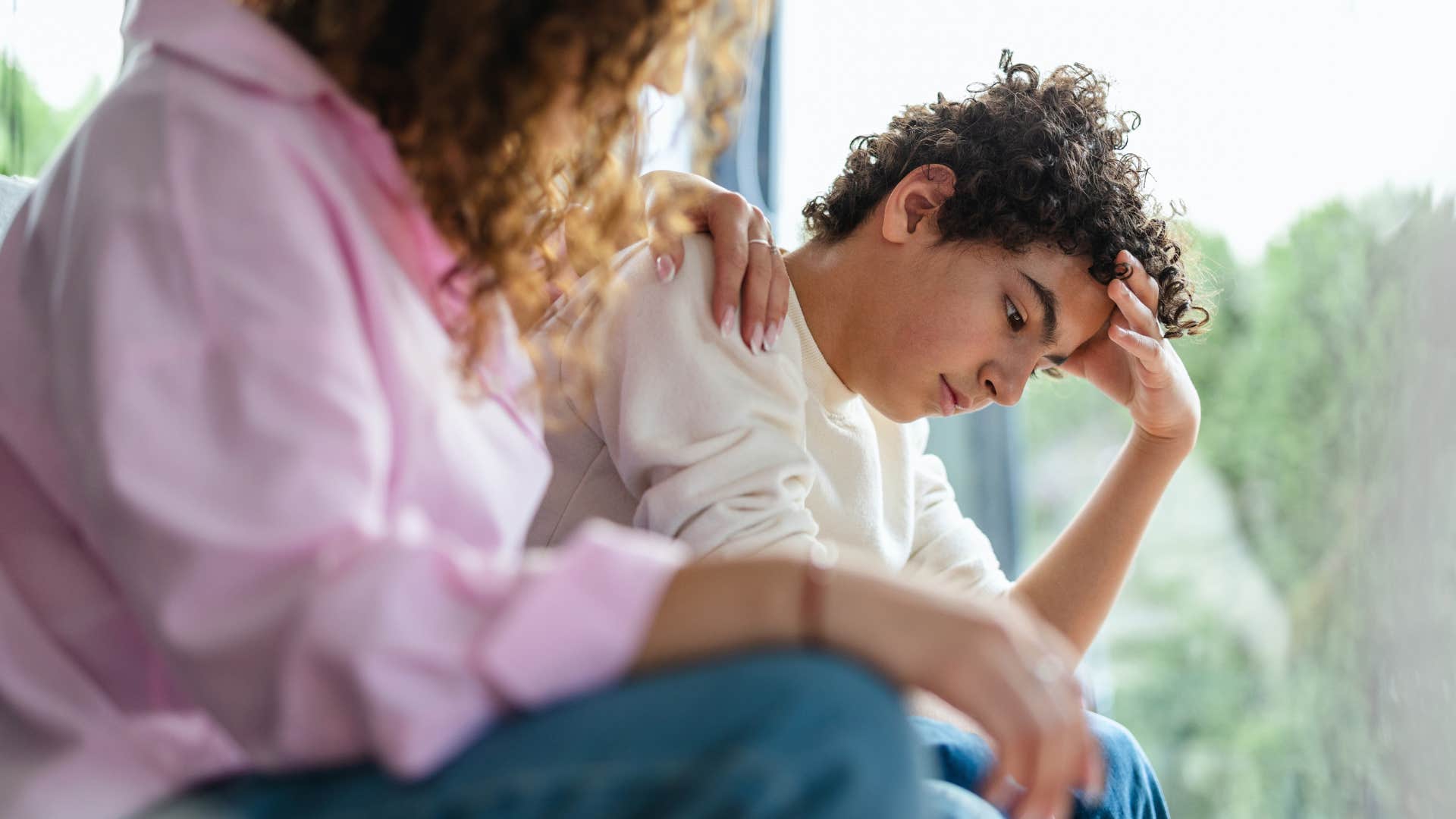 Upset boy sitting with his mom who uses other children as "scapegoats."