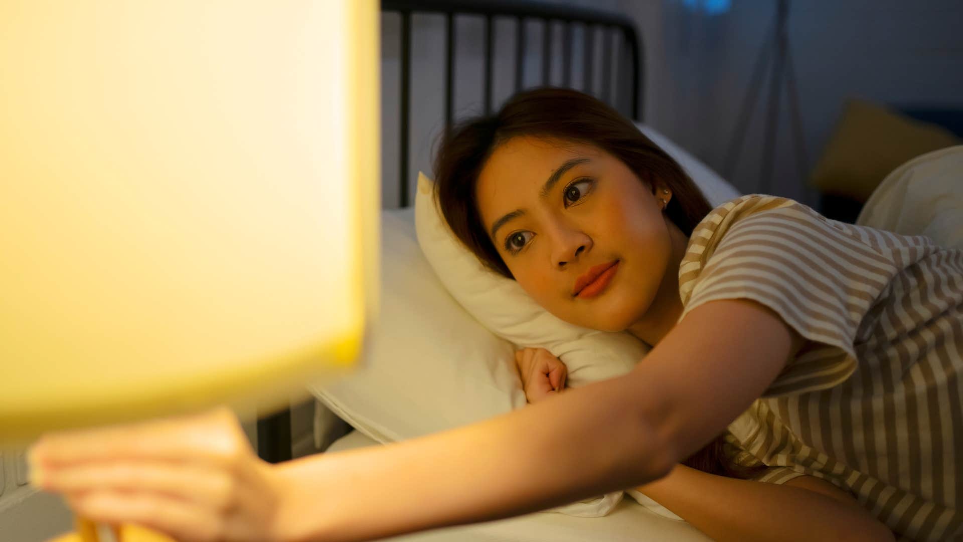 frugal woman in pajamas turning off the lights in bed