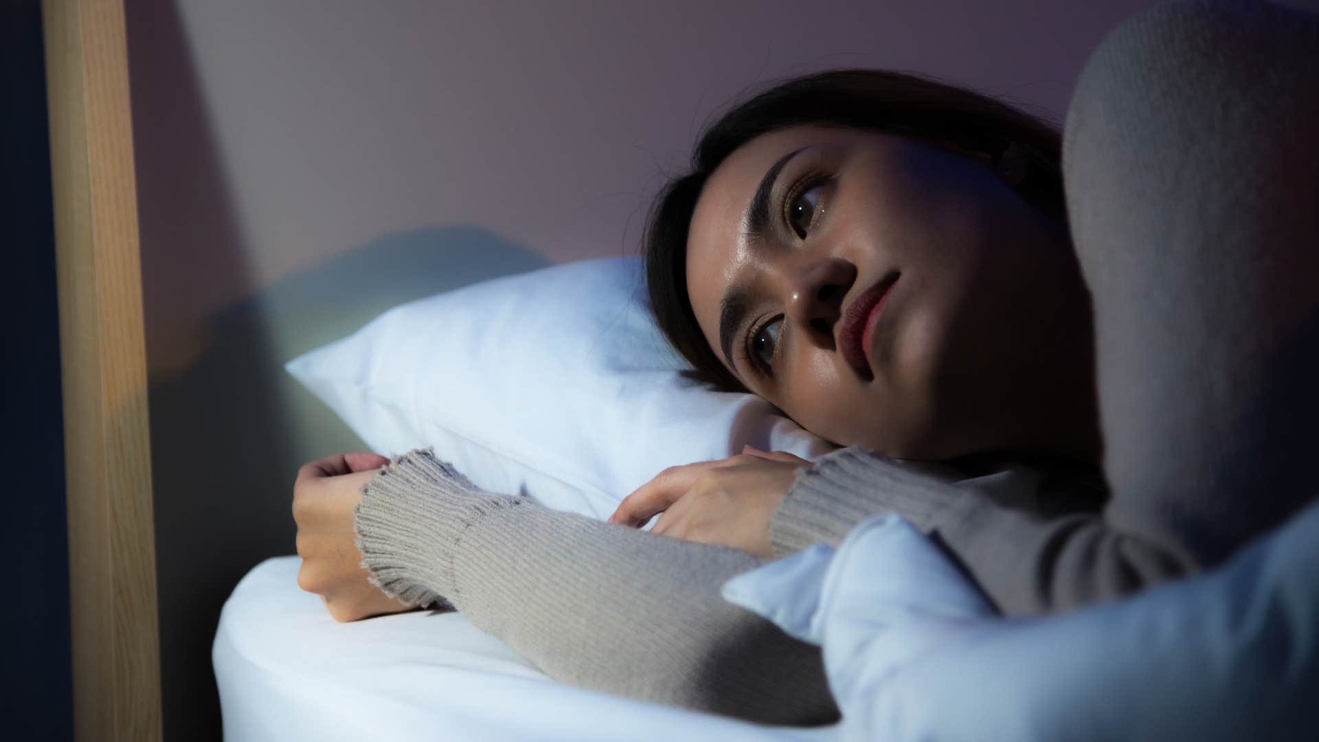 unhappy woman laying in bed with blackout curtains closed