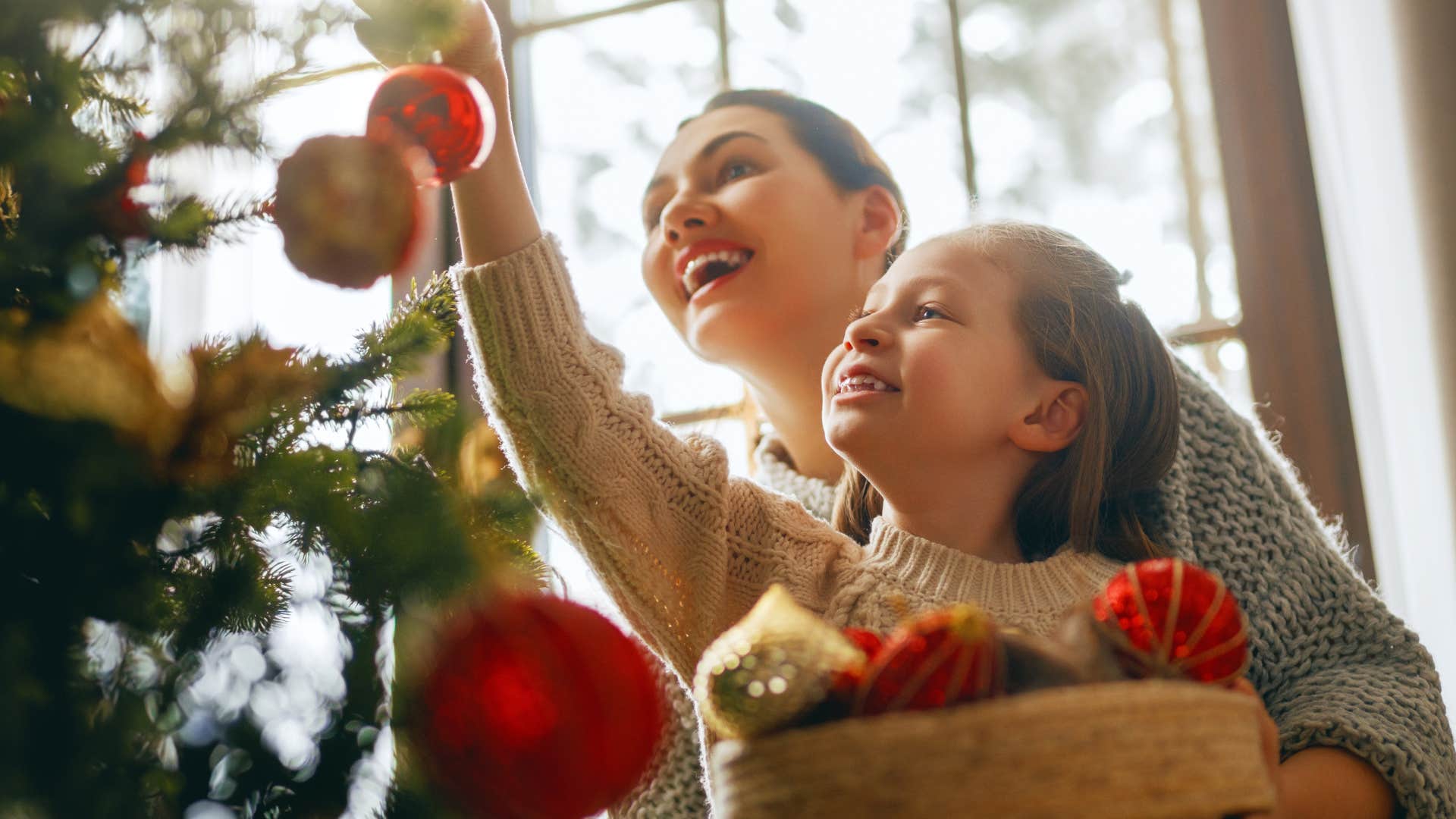 Mother handing up holiday decorations at home with her daughter.