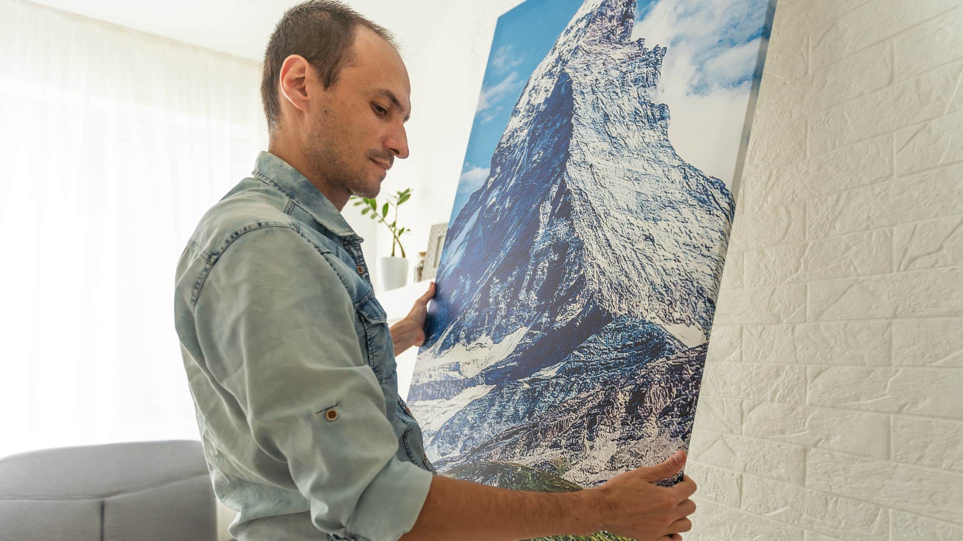 man hanging up artwork at home