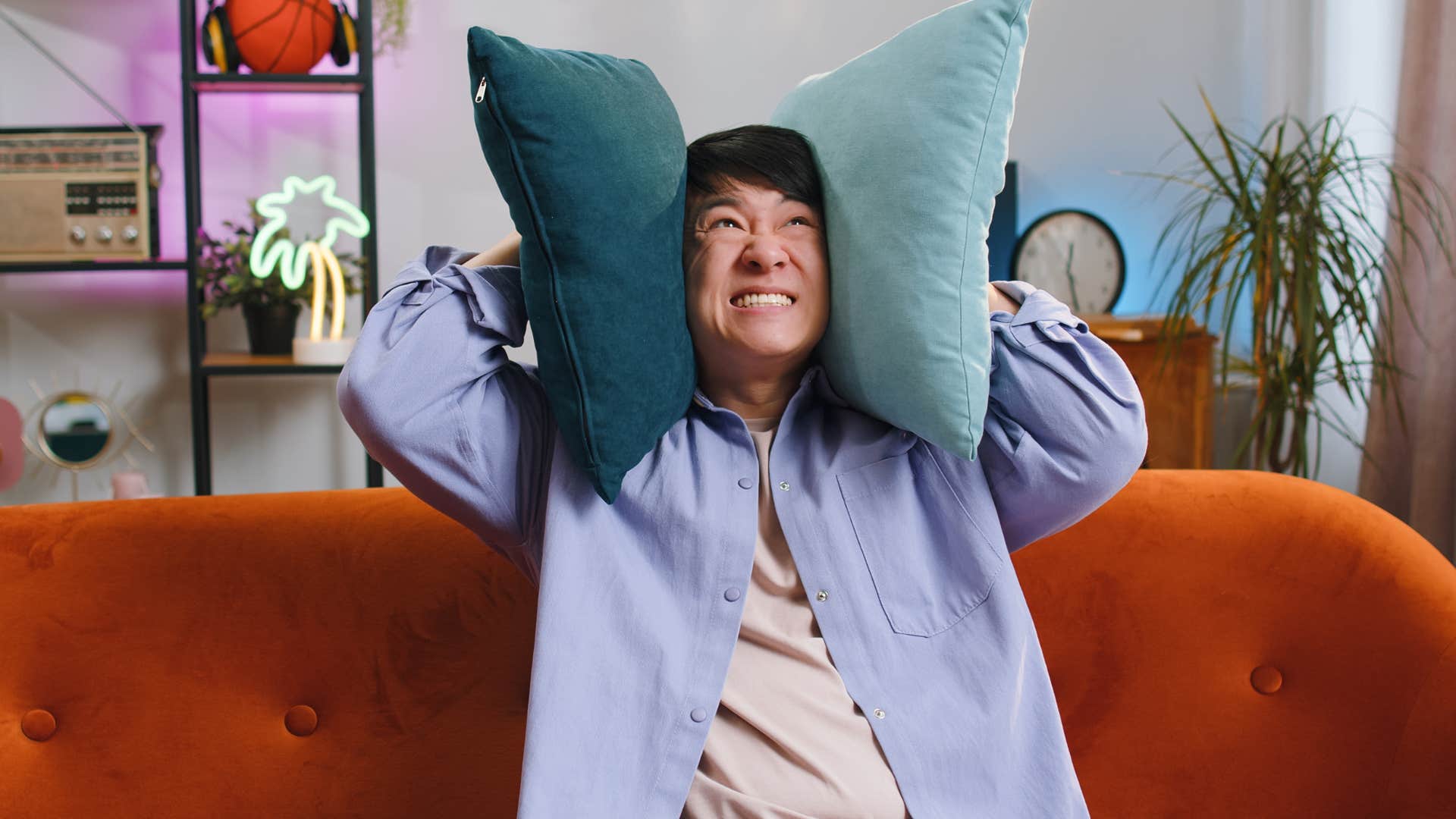 man covering his ears with pillows to block out noise