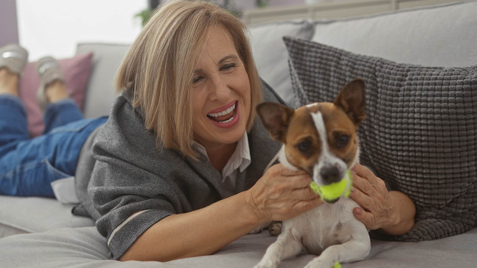 woman laughing with her dog playing with a ball