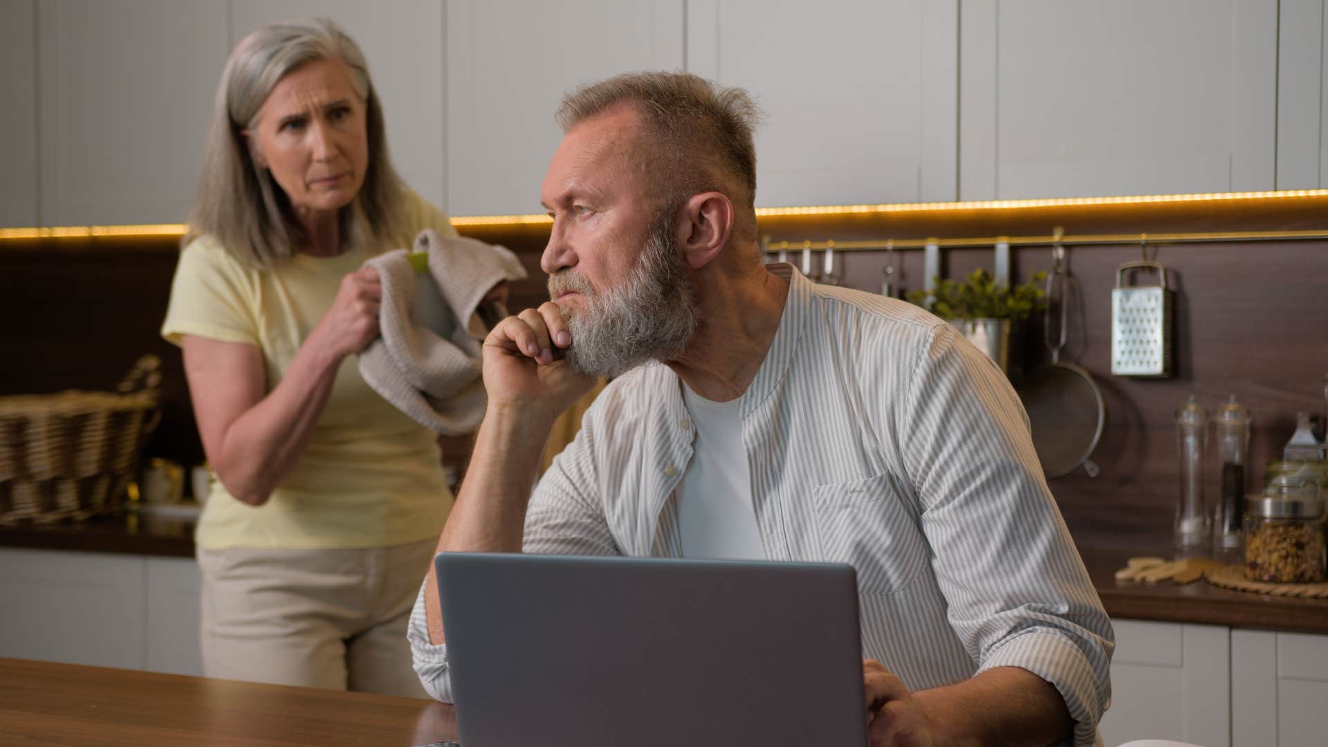 husband busy on laptop with wife talking behind him