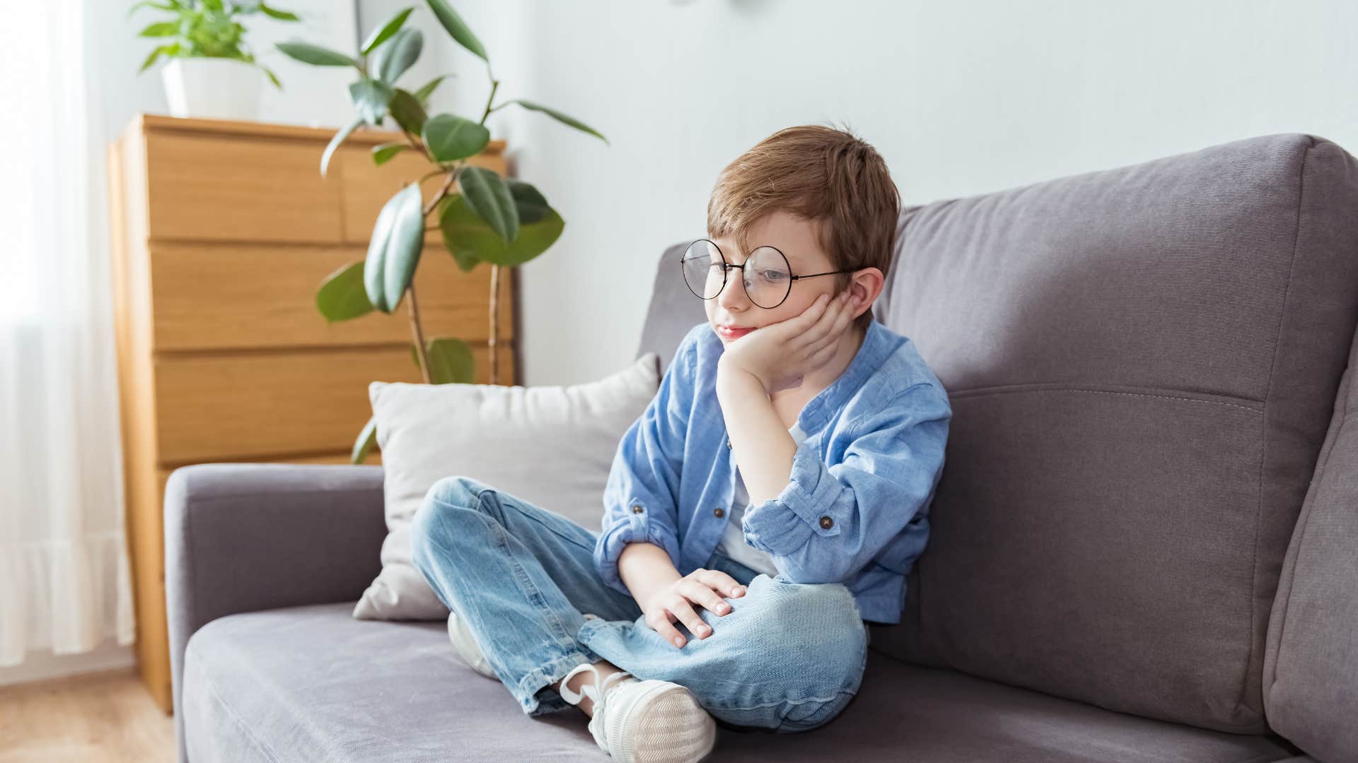 bored little boy sitting on couch saying i dont care to himself