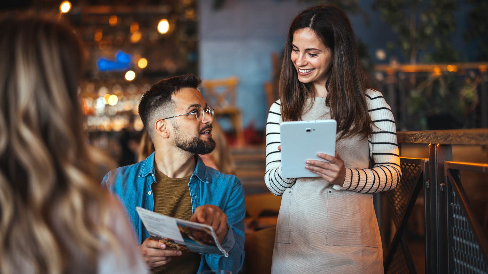 woman insisting man goes first as he orders food while waitress writes it down