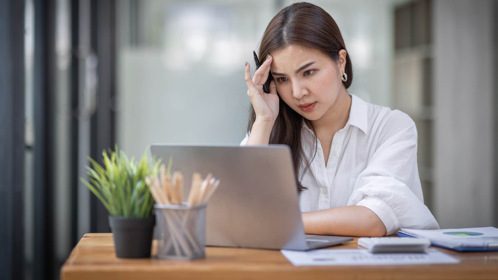 woman in white shirt has her finances in shambles as she stares out laptop stressed