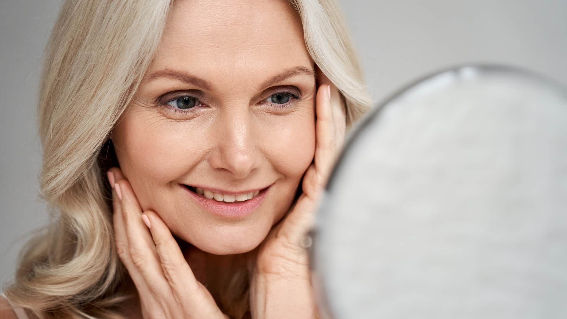 older woman practicing self-care looking in mirror