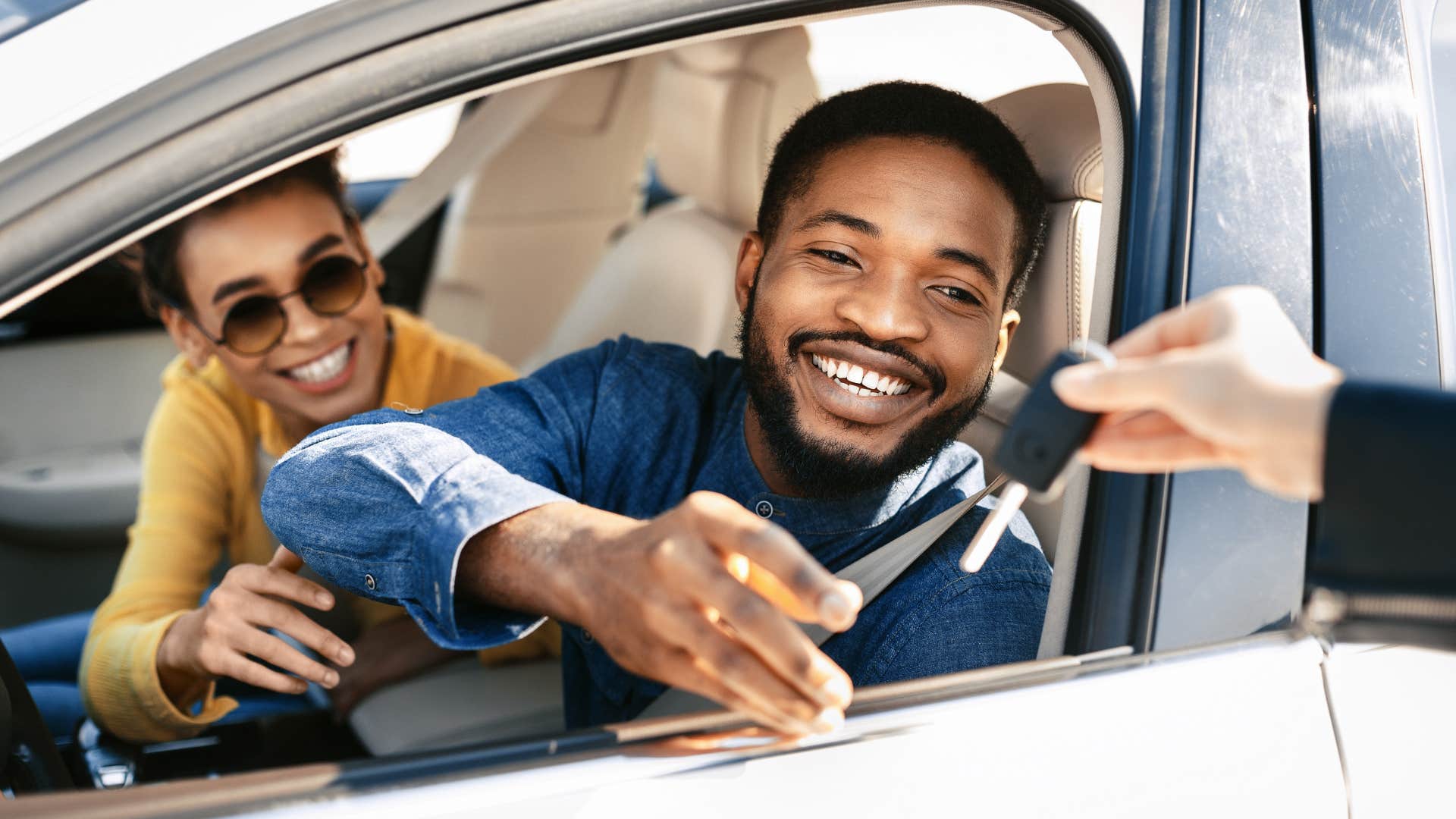 Couple smiling and grabbing the keys for their new cars.