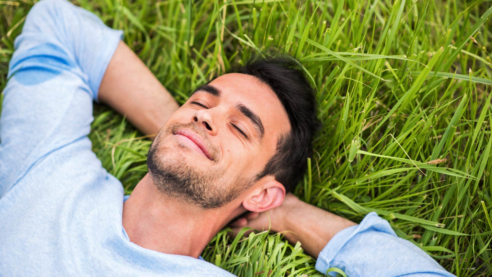 man in blue shirt laying down on the grass while challenging the idea of one life path