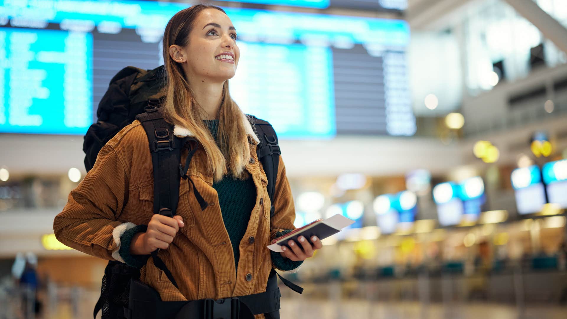 young woman traveling at a young age as she smiles and grips backpack