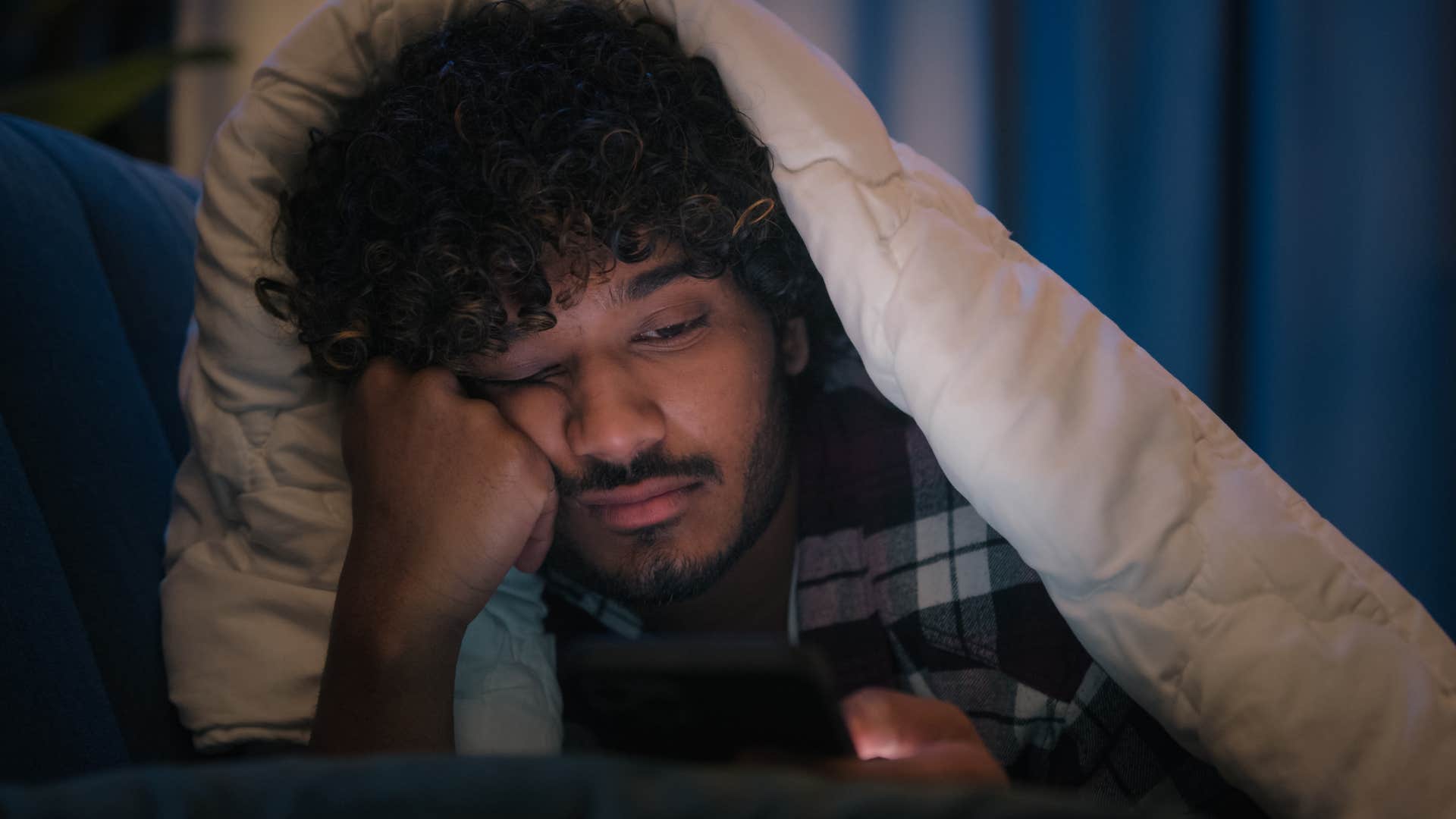 Man doomscrolling on social media from bed.