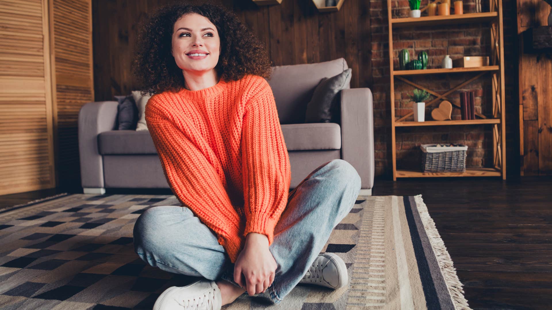Woman smiling and sitting on the flooring at home.
