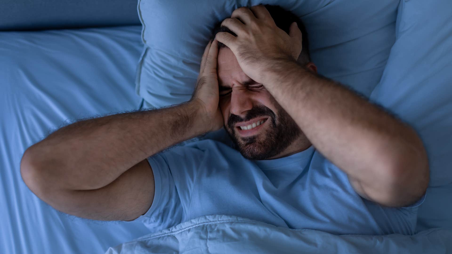Man covering his ears in bed because of noise outside.