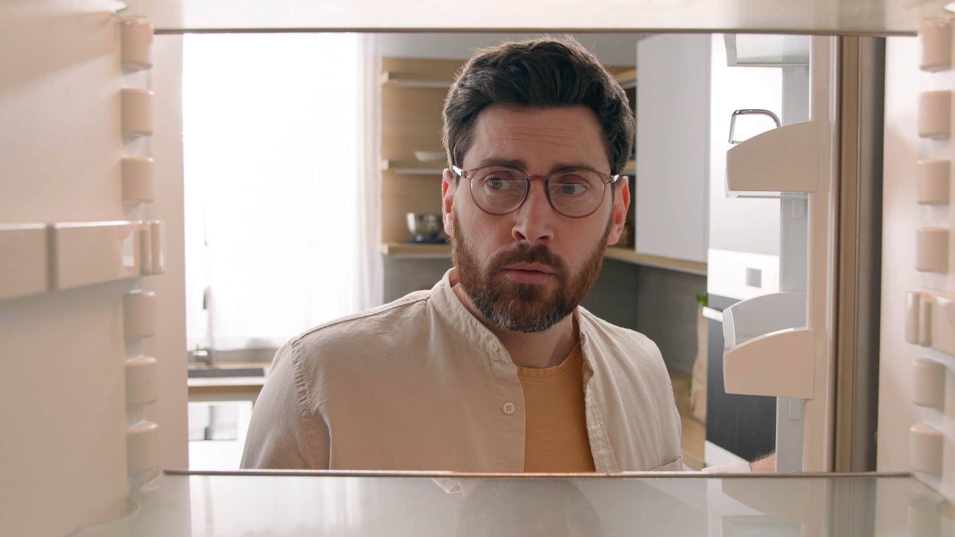Confused man looking in the fridge at home.