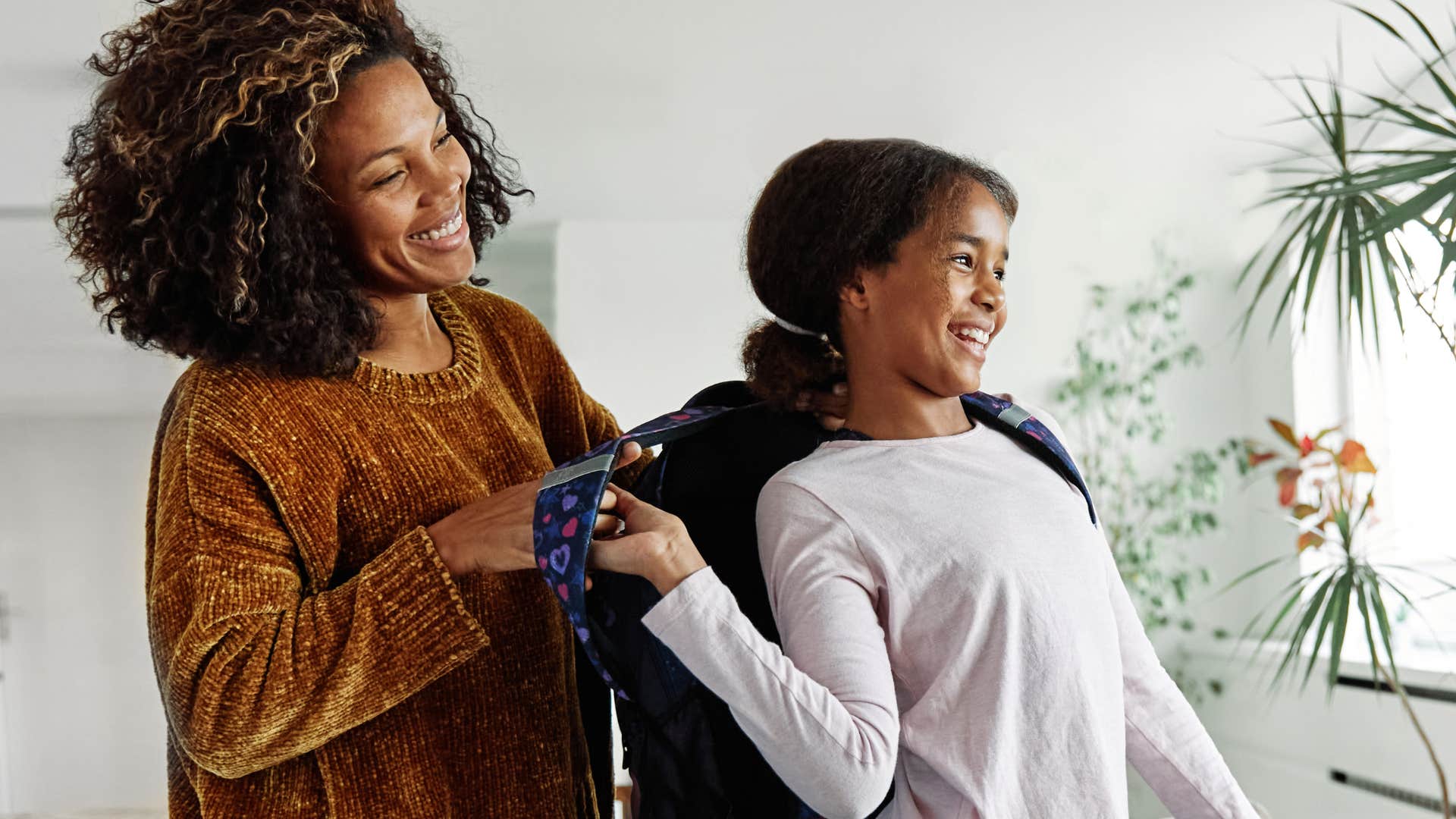 mom putting her daughter's backpack on during the morning rush