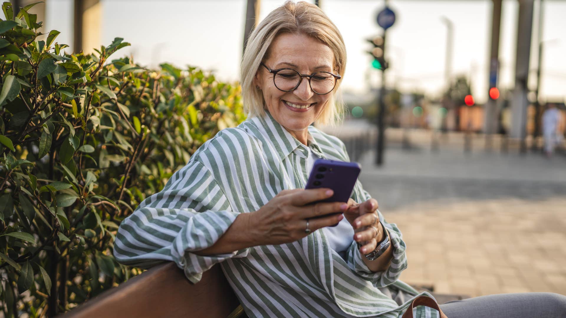Woman smiling and scrolling on Facebook outside.