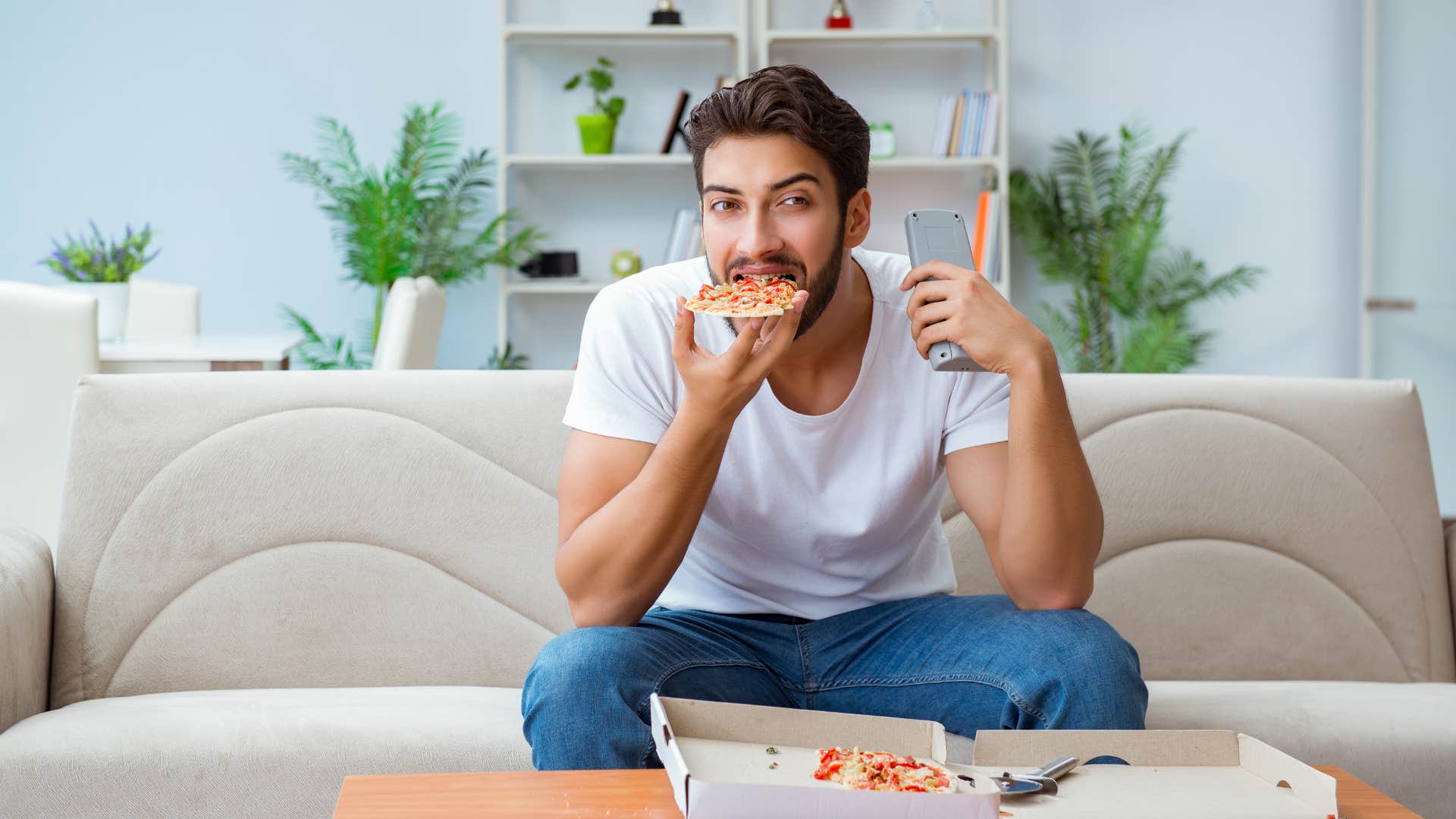 man eating junk food on his couch to save money