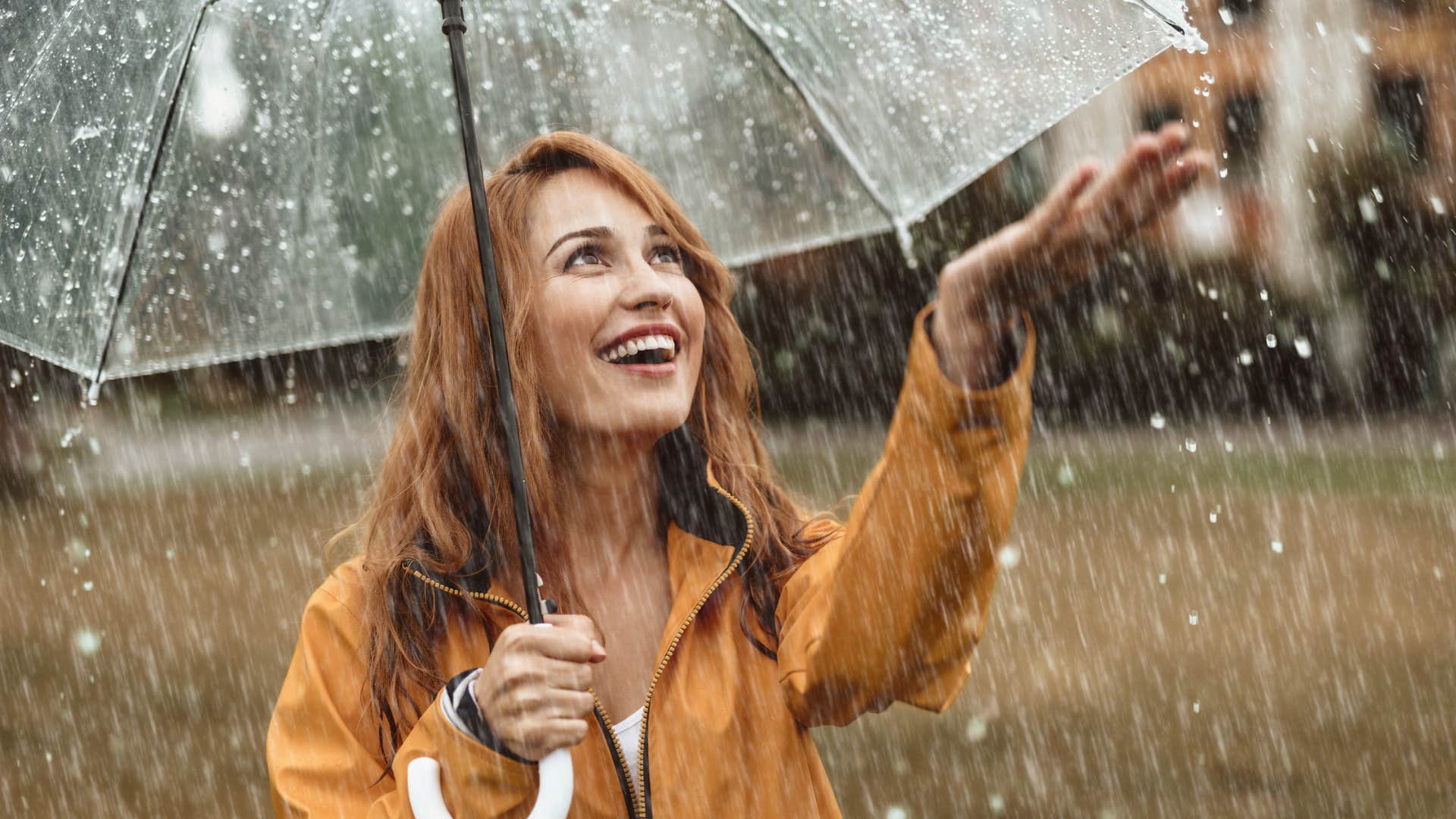 smiling woman unbothered by the rain standing under umbrella