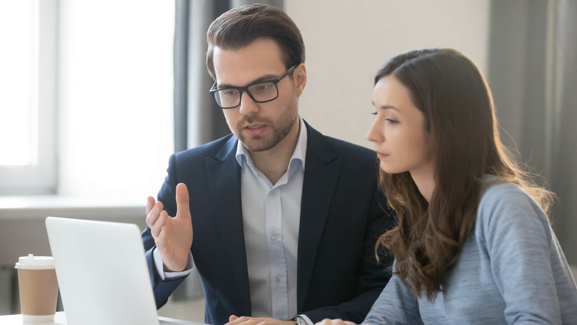 man in suit telling woman no pressure right now but make sure you do this by this date as he points at laptop