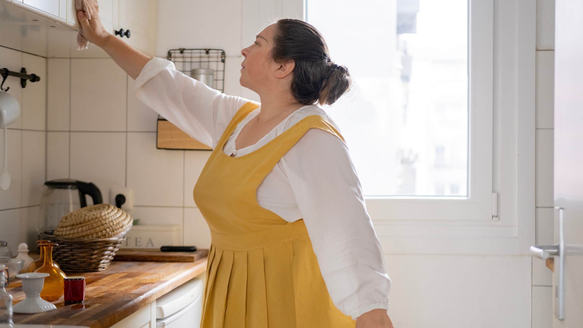woman wiping down counters and cabinets in kitchen